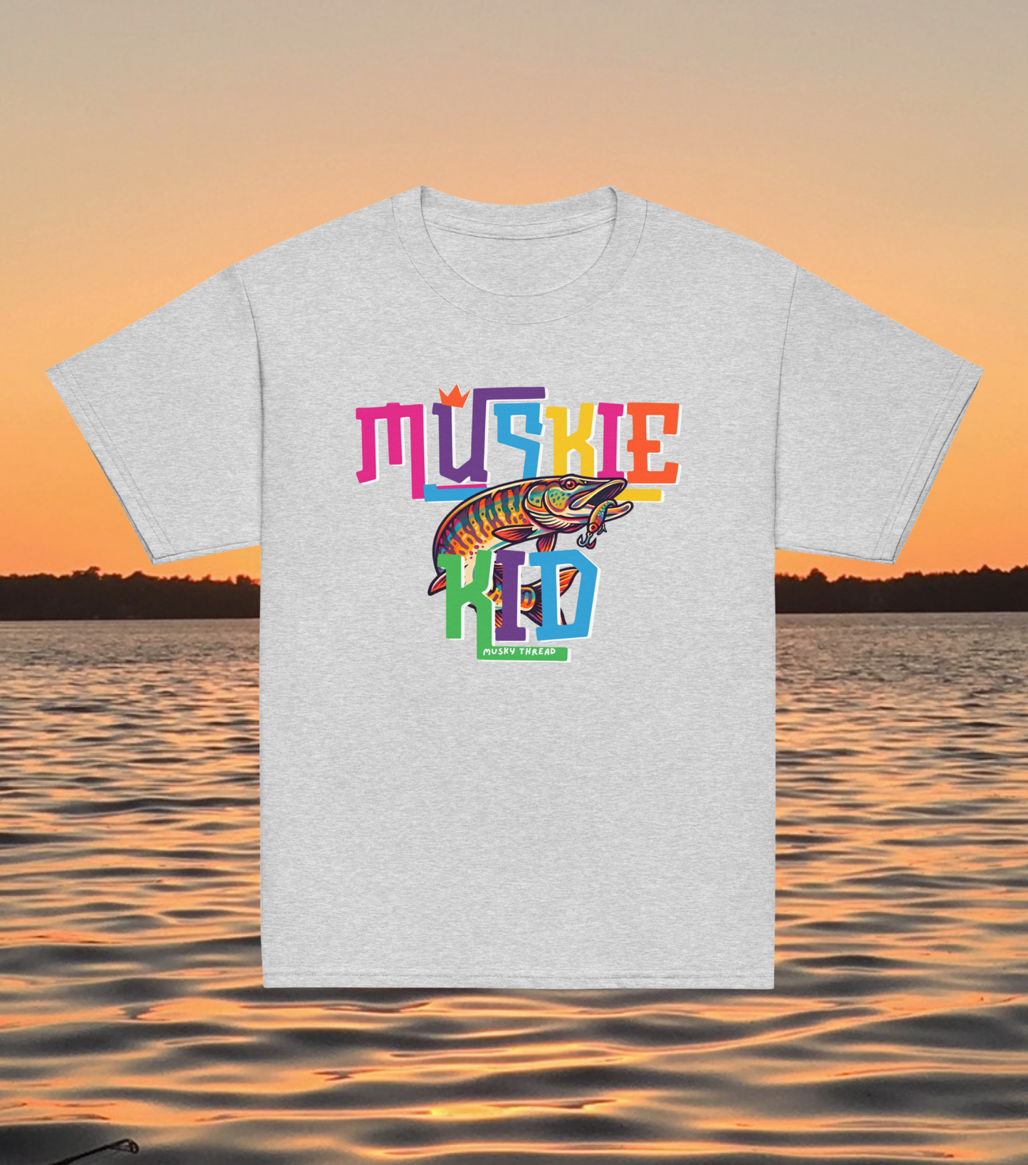 street-style youth graphic t-shirt with colorful hand-lettered Muskie Kid design featuring an illustrated musky fish and crown, displayed against a lake sunset background