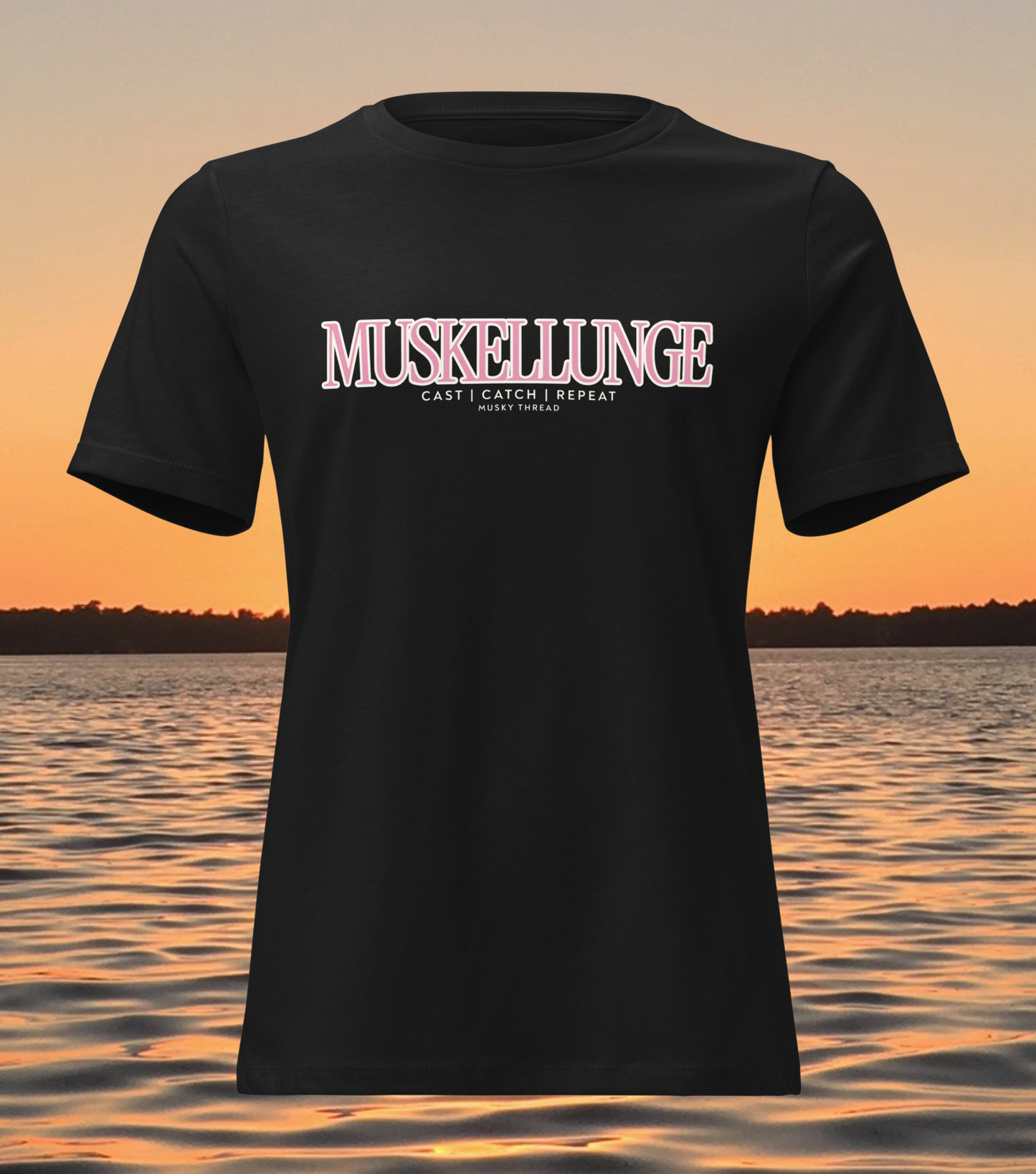 women's t-shirt with pink and white Muskellunge Cast Catch Repeat fishing design, lake sunset background
