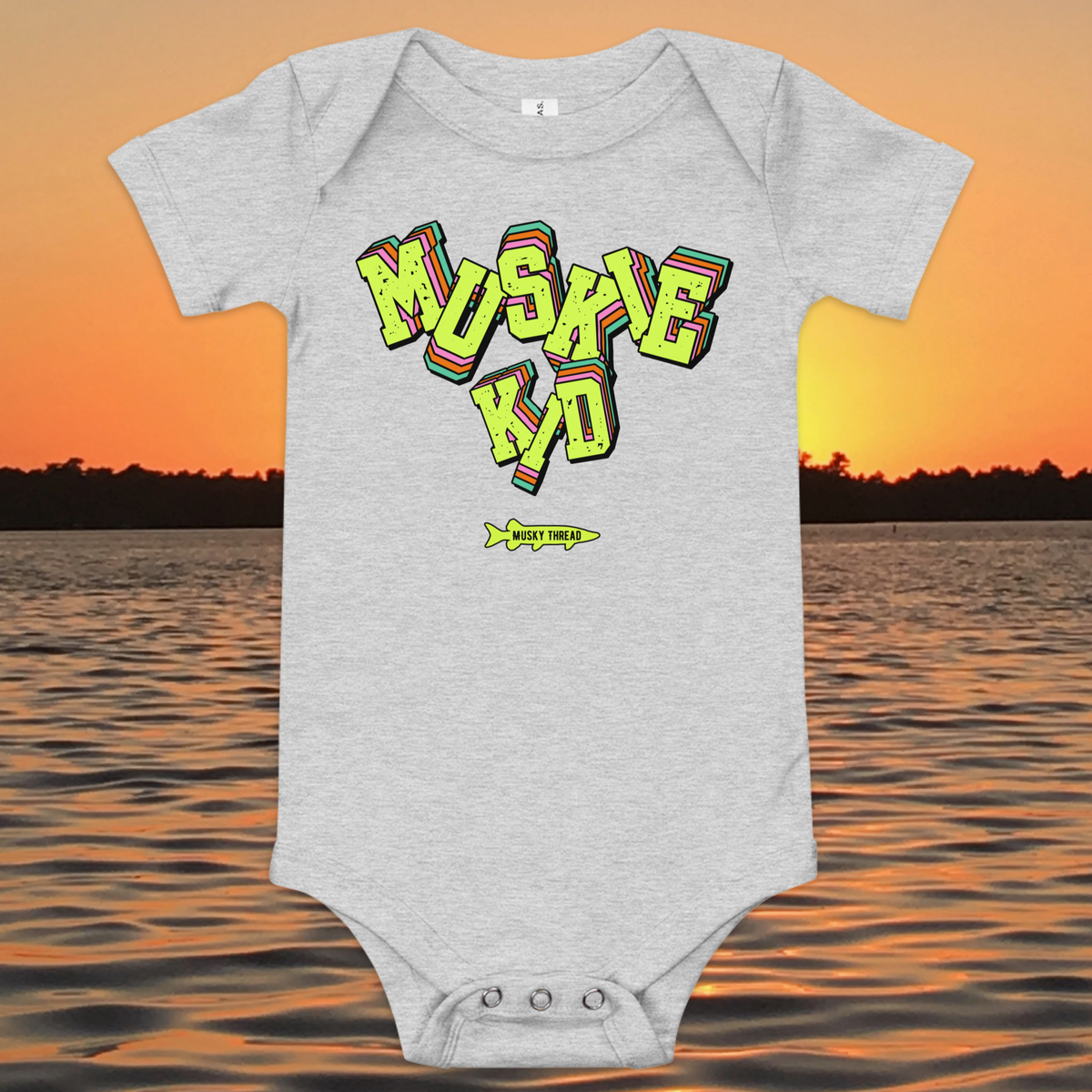 baby one-piece with neon green, pink, and teal "Muskie Kid" retro graphic and Musky Thread fish logo, shown against a lake sunset background