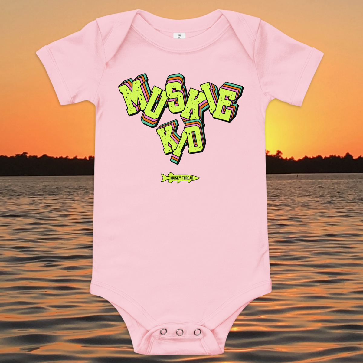 baby one-piece with neon green, pink, and teal "Muskie Kid" retro graphic and Musky Thread fish logo, shown against a lake sunset background