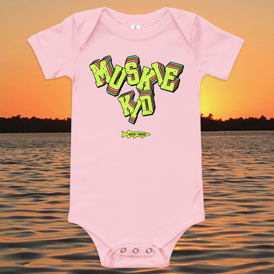 baby one-piece with neon green, pink, and teal "Muskie Kid" retro graphic and Musky Thread fish logo, shown against a lake sunset background