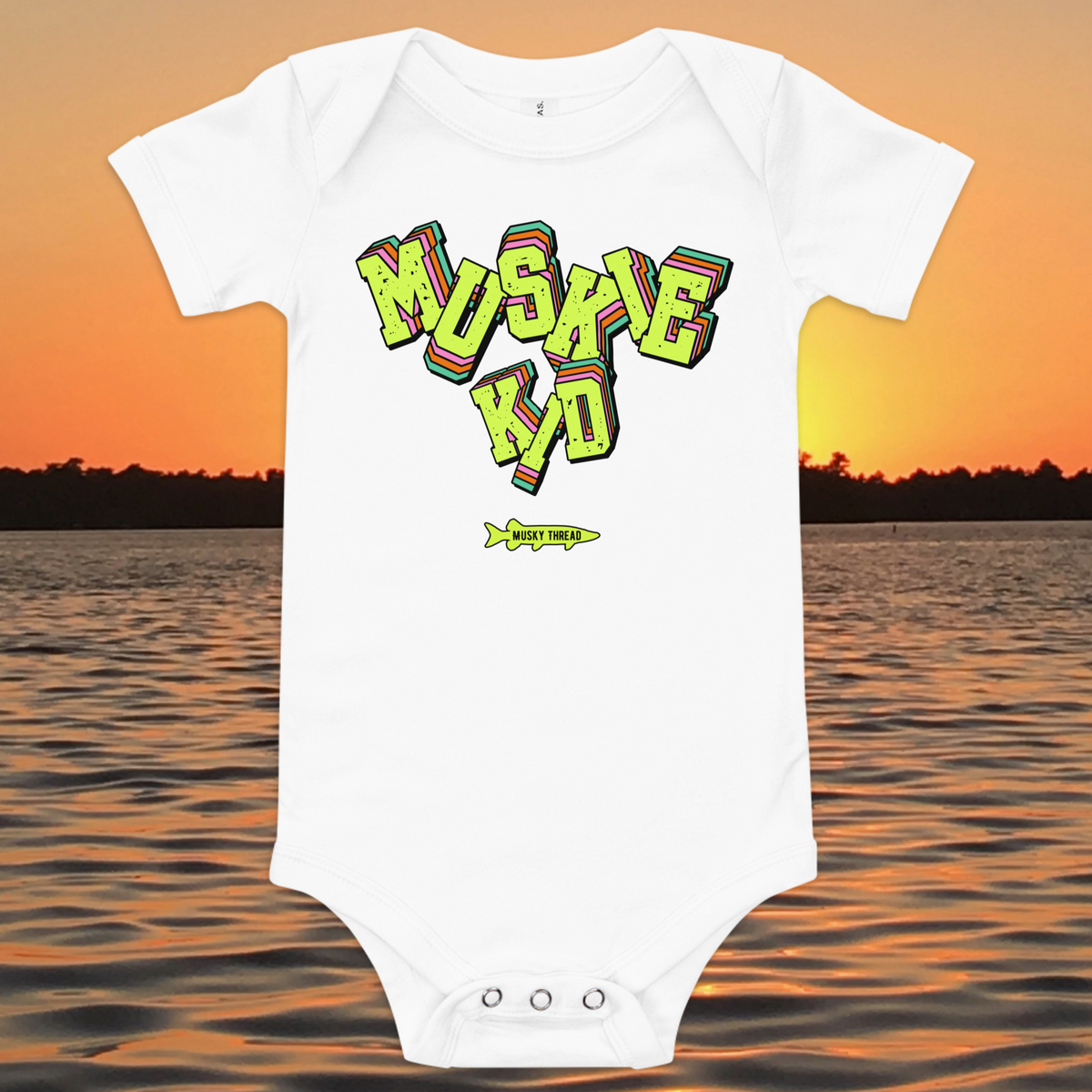 baby one-piece with neon green, pink, and teal "Muskie Kid" retro graphic and Musky Thread fish logo, shown against a lake sunset background