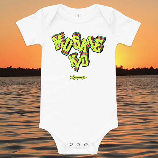 baby one-piece with neon green, pink, and teal "Muskie Kid" retro graphic and Musky Thread fish logo, shown against a lake sunset background