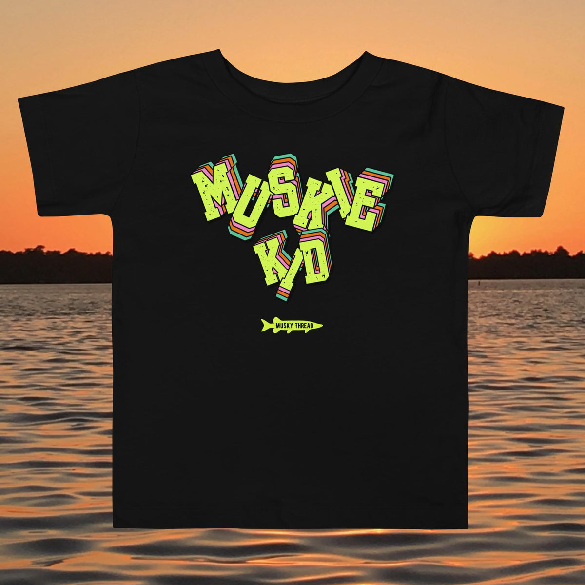 toddler t-shirt with neon green, pink, and teal "Muskie Kid" retro graphic and Musky Thread fish logo, shown against a lake sunset background
