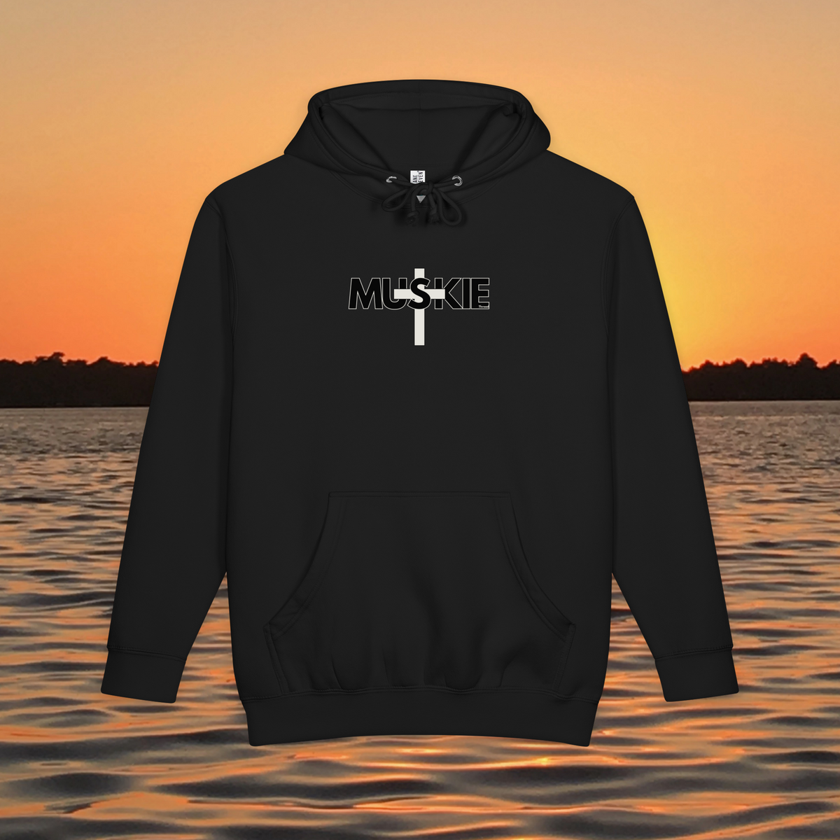 Minimalist Muskie Cross heavyweight pullover hoodie with black MUSKIE lettering crossed by a cream cross, shown over a sunset lake