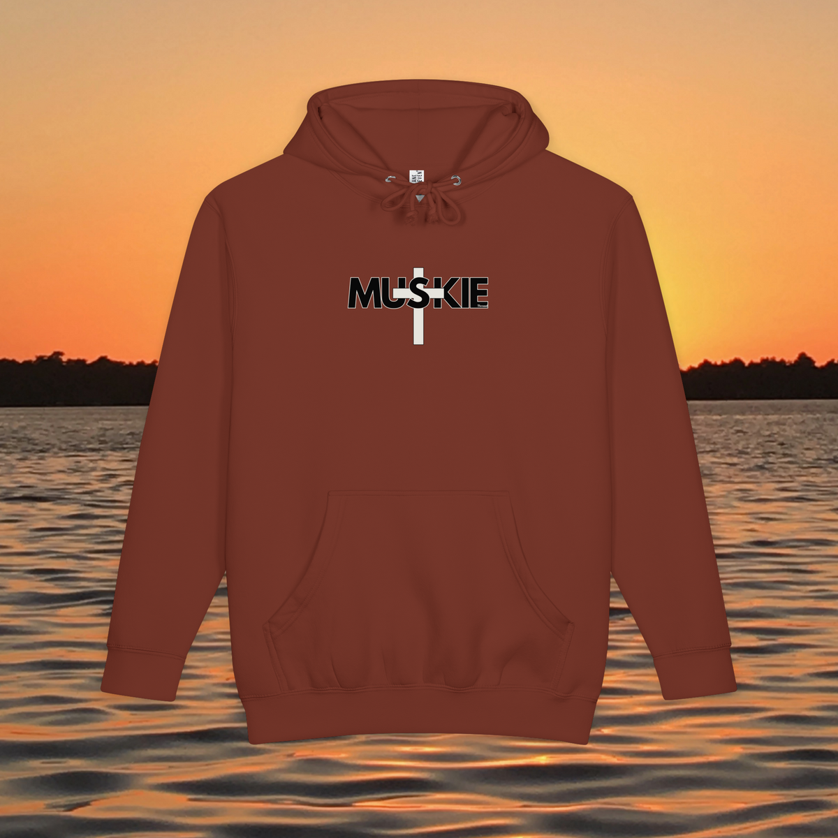 Minimalist Muskie Cross heavyweight pullover hoodie with black MUSKIE lettering crossed by a cream cross, shown over a sunset lake